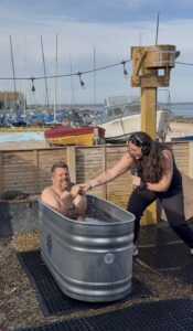 Rob Wills in an ice bath, presenting his experience. With Numi by his side to ensure he doesn't throw his microphone in the water.